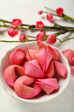 Bir kase pembe fal kurabiyesi ve beyaz arka planda sakura, yakın plan.