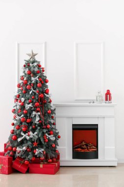 Işık duvarının yanında hediyeler ve şömineyle süslenmiş Noel ağacı.
