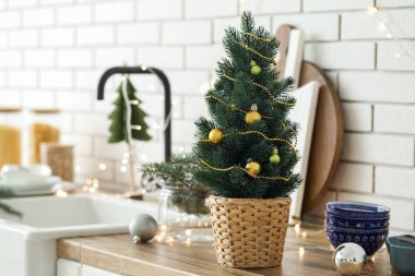 Mutfaktaki beyaz tuğla duvarın yanındaki tezgahta küçük bir Noel ağacı var.