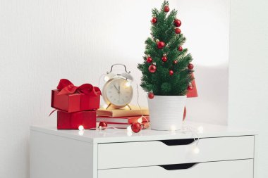 Küçük Noel ağacı, çalar saat, kitaplar, hediyeler ve ışık duvarının yanındaki çekmecelerde parlayan ışıklar.