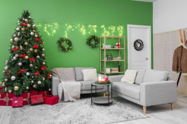 Oturma odasının içinde Noel ağacı, çelenk ve kanepeler var.