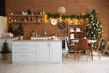 Mutfağın içinde Noel ağaçları, beyaz tezgahlar ve yemek masası var.