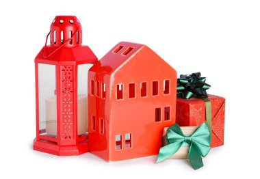 Noel feneri ve beyaz arka planda hediyeler olan ev şeklinde mumluk.