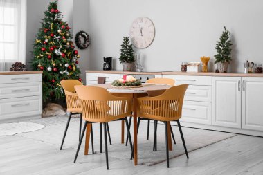 Mutfağın içinde Noel ağaçları, beyaz tezgahlar ve yemek masası var.