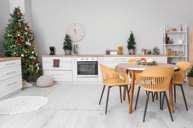 Mutfağın içinde Noel ağaçları, beyaz tezgahlar ve yemek masası var.