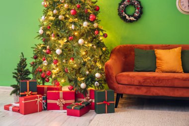 Oturma odasının içinde Noel ağacı, kanepe, çelenk ve parlayan ışıklar var.