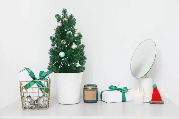 stock image Small Christmas tree with presents, candles and mirror on shelf near light wall