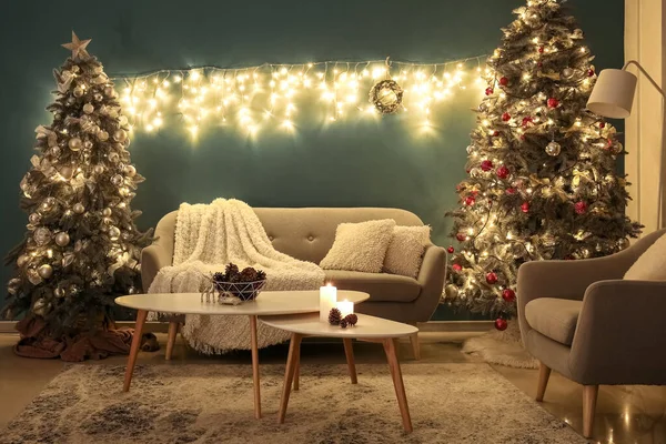 Interior of dark living room with Christmas trees, sofa and glowing lights