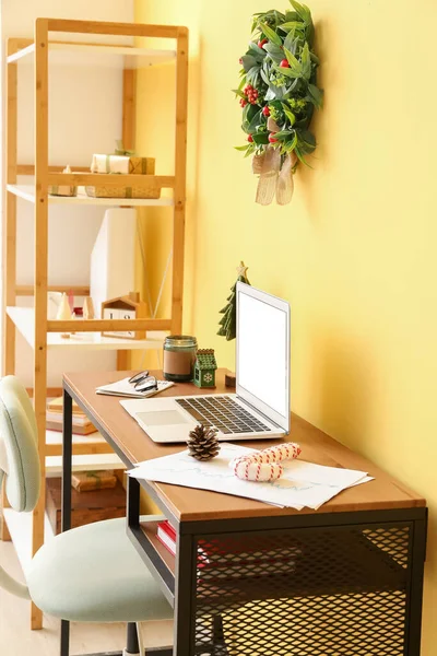 办公室靠近黄墙的桌面上挂着圣诞玩具和蜡烛的笔记本电脑 — 图库照片