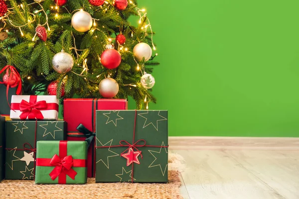 緑の壁の近くに輝くクリスマスツリーの下の贈り物 — ストック写真