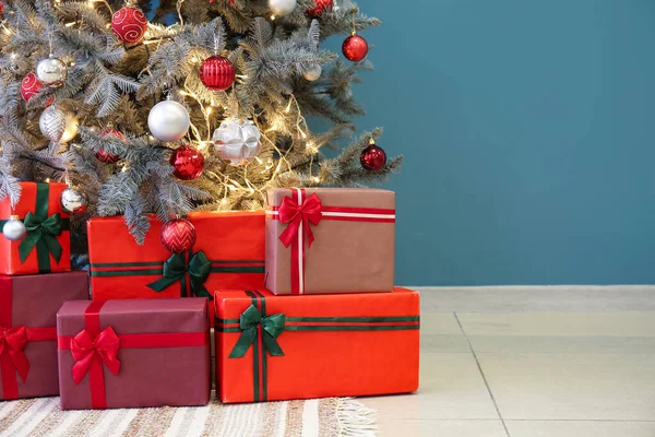 青い壁の近くの輝くクリスマスツリーの下の贈り物 — ストック写真