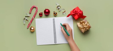 Kadın el yazısı boş defterde, Noel hediyeleri ve renkli arka planda toplar.