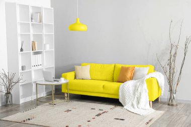 Sarı kanepe, lamba ve raf ünitesiyle aydınlık oturma odasının içinde.