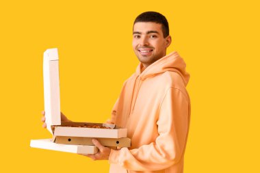 Sarı arka planda taze pizza kutuları tutan yakışıklı genç adam.
