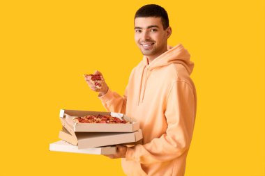 Sarı arka planda taze pizza kutuları tutan yakışıklı genç adam.