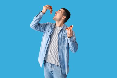 Yakışıklı genç adam mavi arka planda taze pizza yiyor.