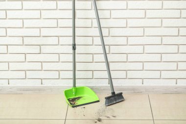 Çöplü faraş ve tuğla duvarın yanındaki süpürge.
