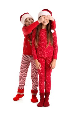 Noel Baba şapkalı küçük çocuk beyaz arka planda kız kardeşinin gözlerini kapatıyor.