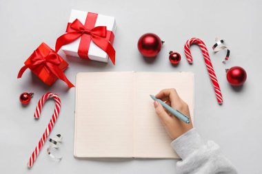Boş defter, kalem, Noel hediyeleri ve arka planda süslemeleri olan kadın eli
