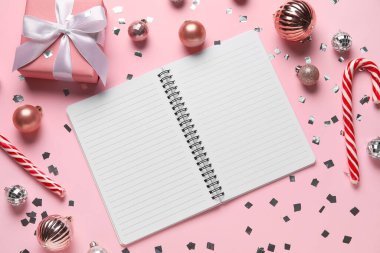 Boş defter, baston şekerler ve pembe arka planda Noel süslemeleri olan kompozisyon