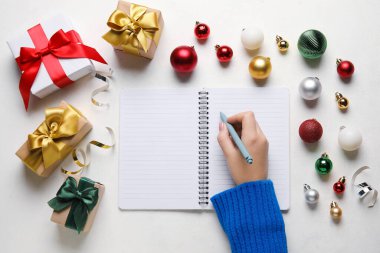 Boş defter, kalem, Noel hediyeleri ve arka planda topları olan bir kadın eli.