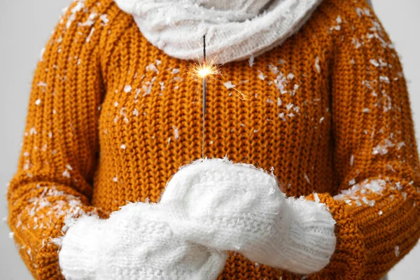 Woman in mittens with Christmas sparkler on grey background, closeup