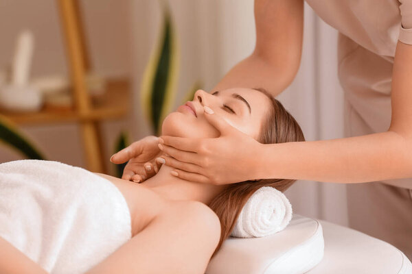 Pretty young woman receiving face massage in beauty salon