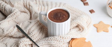 Bir fincan sıcak çikolata, örgü süveter ve beyaz masada kurabiyeler.