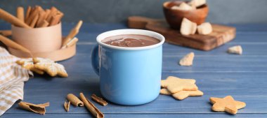 Bir fincan sıcak çikolata, tarçın ve ahşap masada kurabiyeler.