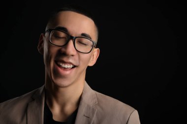 Siyah arka planda gözleri kapalı, gözlüklü gülümseyen Asyalı adam.