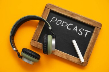 PODCAST sözcüğü ve turuncu arka planda kulaklıkları olan yazı tahtası