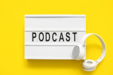 Sarı arka planda PODCAST ve kulaklıkları olan tahta