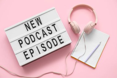Pembe arka planda NEW PODCAST EPISODE, not defteri ve kulaklıkları olan tahta