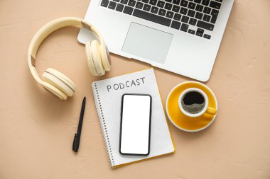 Kelime PODCAST, cep telefonu, kulaklık, kahve fincanı ve bej arka planda dizüstü bilgisayarlı defter