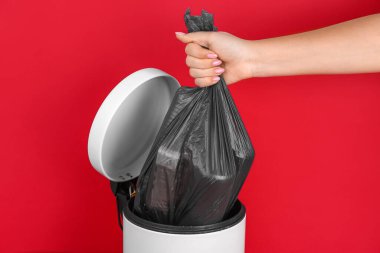 Kırmızı arka plandaki çöp kutusundan çöp torbası çıkaran kadın.