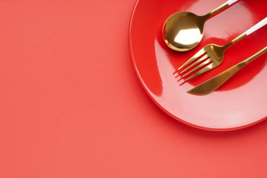 Kırmızı arka planda çatal bıçak takımı olan kırmızı tabak.