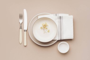 Bej arka planda beyaz tabak, peçete ve çatal bıçak.