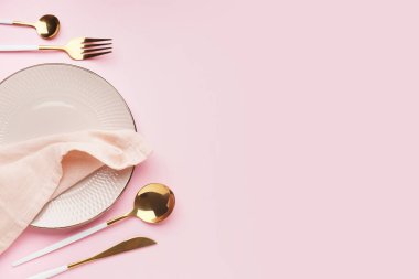 Pembe arka planda peçete ve çatal bıçak takımı olan beyaz tabak.
