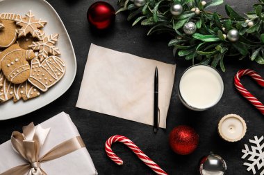 Noel Baba 'ya bir bardak süt, kurabiye ve siyah arka planda Noel dekoruyla boş bir mektup.