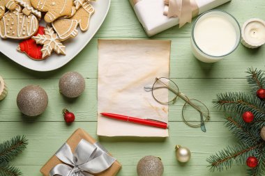 Noel Baba 'ya gözlüklü, Noel dekorlu, kurabiyeli ve yeşil ahşap arka planda bir bardak sütle boş bir mektup.