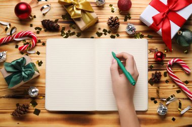 Boş defter, kalem, Noel hediyeleri ve ahşap arka planda süslemeleri olan kadın eli.