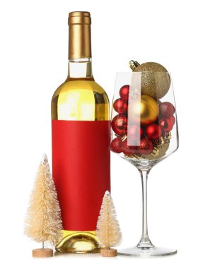 Bir şişe şarap, beyaz arka planda Noel topları ve köknar ağaçları.