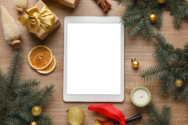 Blank tablet computer with Christmas decor, gifts and citruses on wooden background