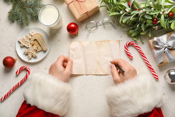 Santa Claus with blank letter, glass of milk, cookies and Christmas gifts on white background