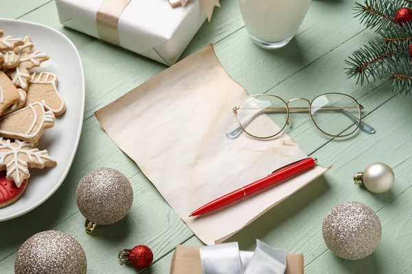Noel Baba 'ya gözlüklü, Noel dekorlu, kurabiyeli ve yeşil ahşap arka planda bir bardak sütle boş bir mektup.