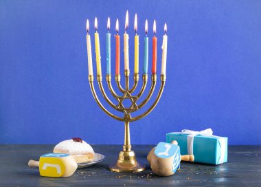 Hannukah kutlaması için donutlu, hediyeli ve mavi duvarın yanındaki masada duran Menorah.
