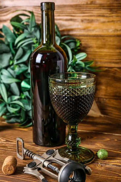 Bottle of wine, glass, opener and Christmas wreath on wooden table, closeup