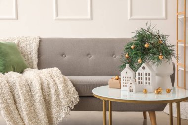 Noel dalları, toplar ve ev şeklinde mum tutacakları olan vazolar oturma odasındaki masada.