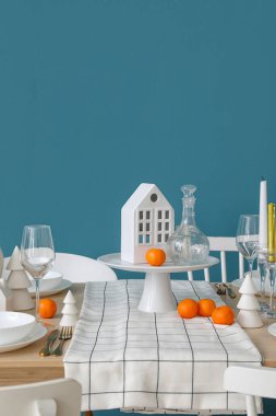 Mavi duvarın yanında mum tutacaklı ve mandalinalı Noel masası.