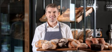 Dükkanında taze ekmek çeşitleriyle mutlu bir erkek fırıncı.